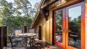 Een houten terras met een tafel, stoelen, een glazen deur en uitzicht op bomen.