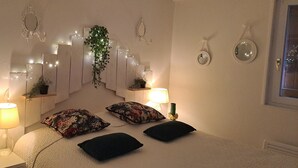 Un dormitorio con una cama, dos mesitas de noche, dos lámparas, un espejo e iluminación decorativa en la pared.