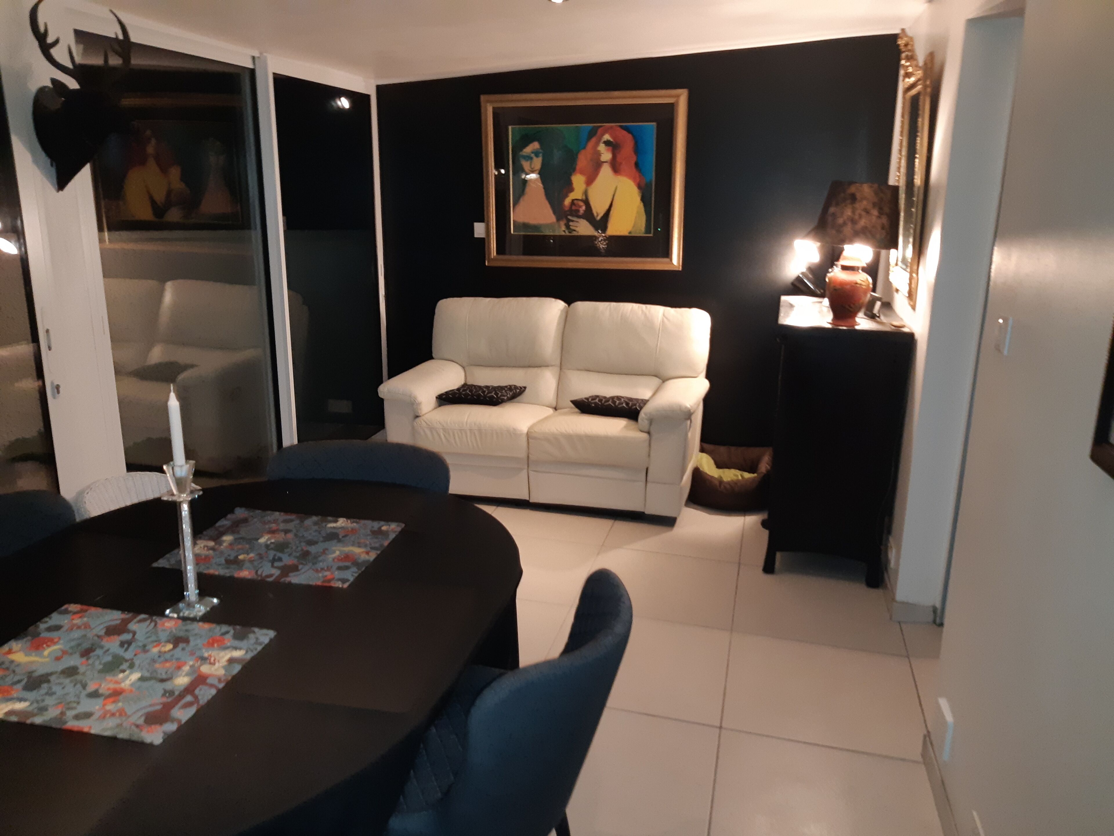 Un soggiorno con un divano bianco, un tavolo da pranzo con tovaglia decorata e un quadro appeso al muro.