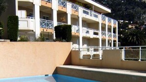 Une piscine entourée de rampes métalliques, bordée d’un mur beige et d’un immeuble à plusieurs étages doté de balcons.