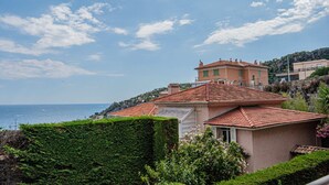 Une maison située sur la côte, avec un toit en tuiles, entourée de verdure et offrant une vue sur la mer.