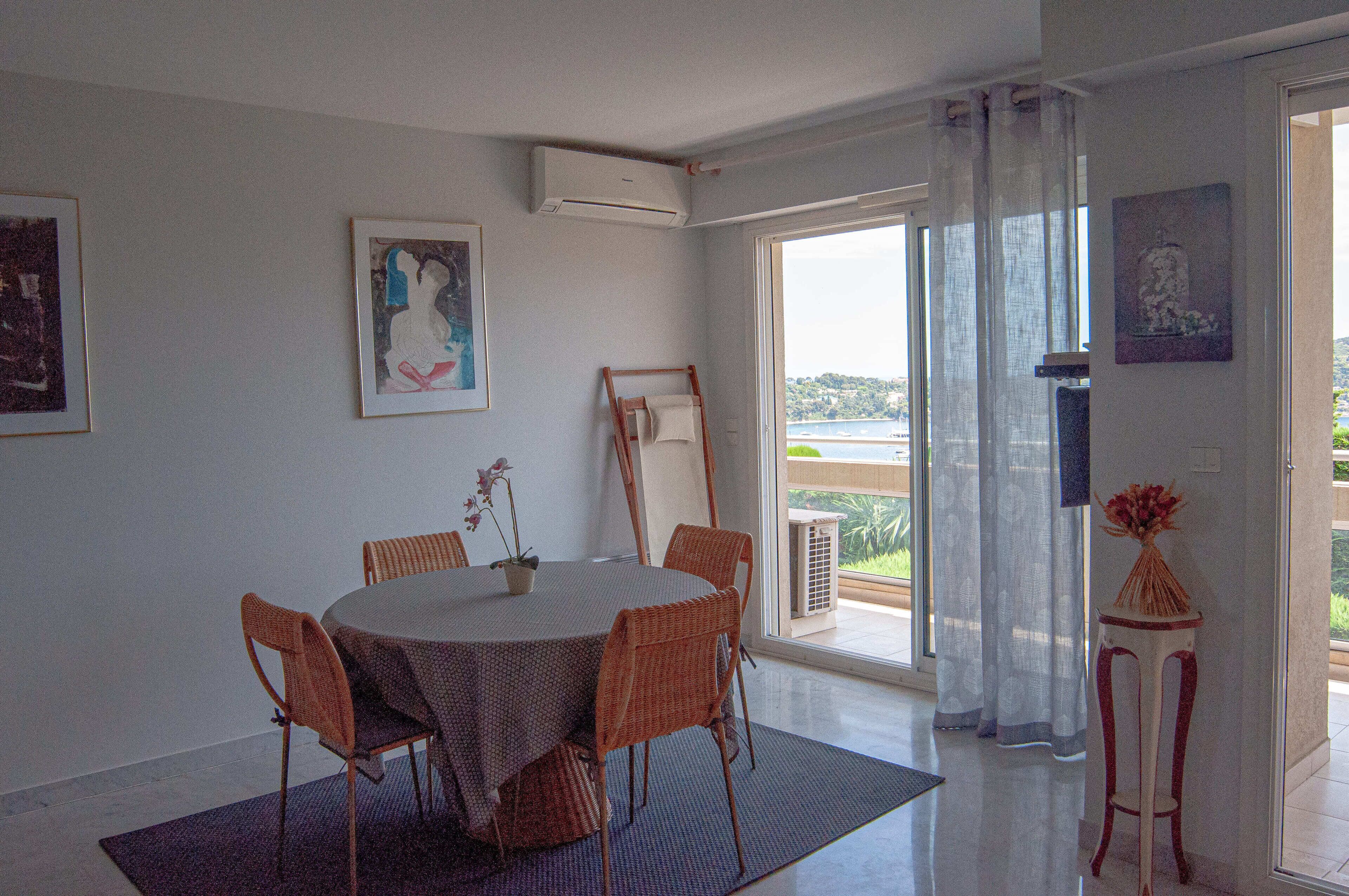 Un coin repas avec une table ronde, des chaises en osier et une vue sur un balcon doté d’une balustrade.