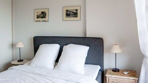 Un lit bien fait, avec du linge de lit blanc, deux tables de chevet avec des lampes et deux tableaux encadrés accrochés au mur.