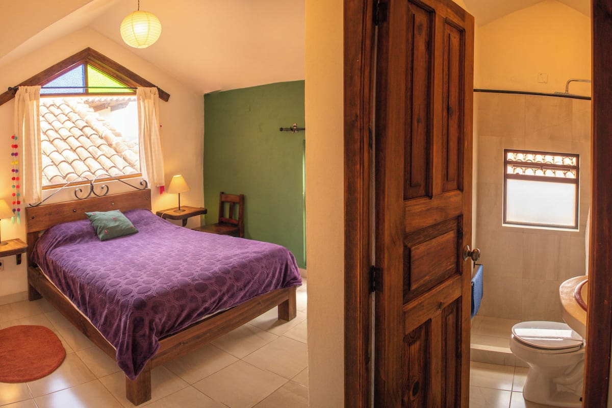Un dormitorio con cama, ventana con cortinas, mesita de noche y lámpara de noche.