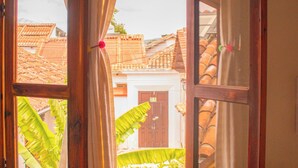 Una ventana abierta con cortinas, una mesa de madera y vista a una casa con tejado de tejas.