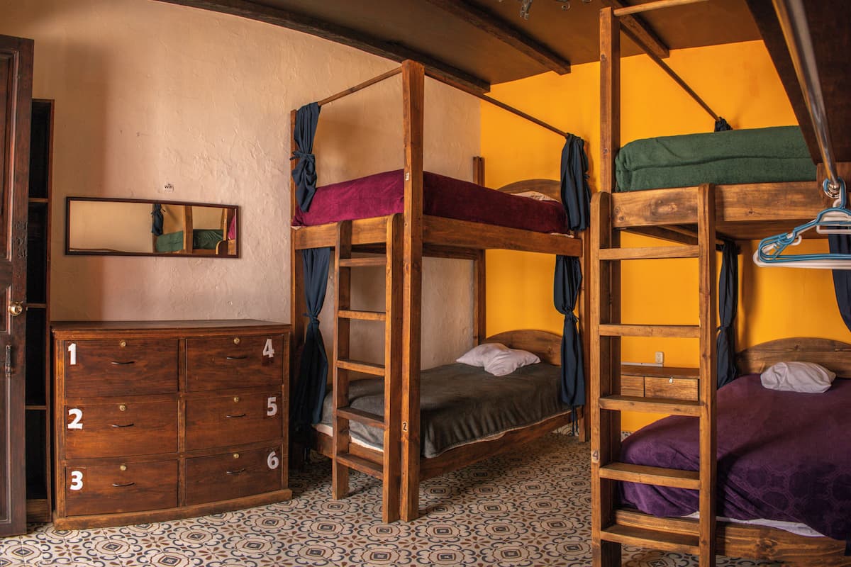 Una habitación con literas, un aparador con cajones, un espejo y baldosas de suelo estampadas.