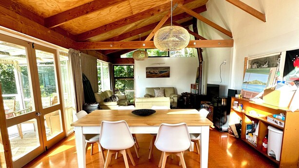A spacious kitchen with a wooden ceiling, large windows, and a dining area with white chairs.