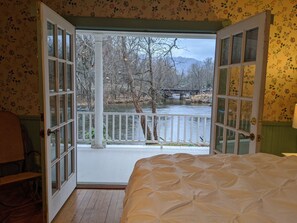 A room with a bed, a chair, and a view of a river and bridge.