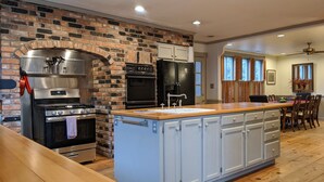 A kitchen with a brick wall, stainless steel appliances, a wooden island, and a dining area with a view of trees. - Southern charm Riverside (Bryson City)