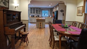 A dining area with a wooden table and chairs, a piano, and a kitchen in the background. - Southern charm Riverside (Bryson City)
