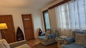 A living room with a wooden door labeled "Beach House Master Bedroom," a blue armchair, a glass coffee table, and a lamp.