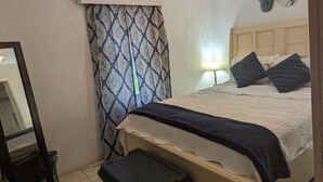 A bedroom with a bed, a nightstand, a lamp, a mirror, and a patterned curtain.
