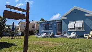 A house with a blue exterior, a front porch with white chairs, and a sign that reads "Local Appetizer."
