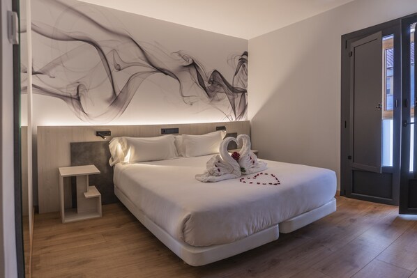 Une chambre moderne avec un grand lit, une table de chevet, une lampe fixée au mur et une porte sur le côté droit.