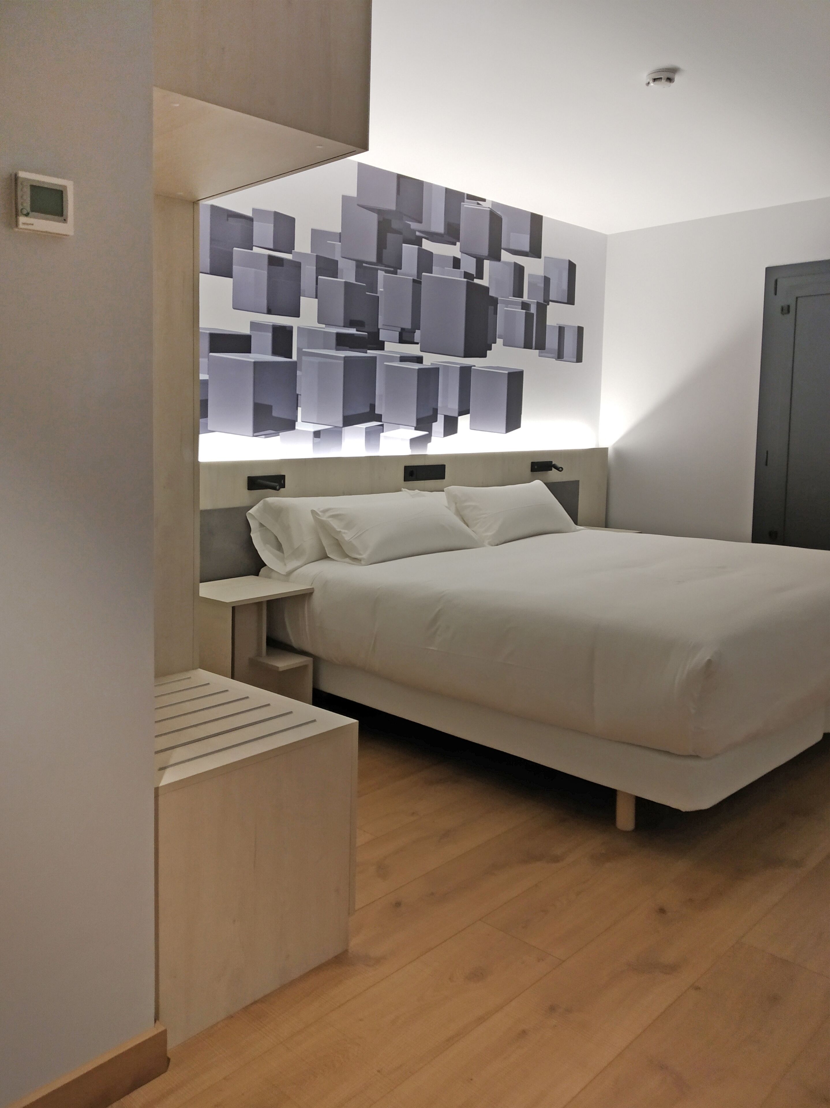Un dormitorio moderno con cama, mesitas de noche y una lámpara de pared.