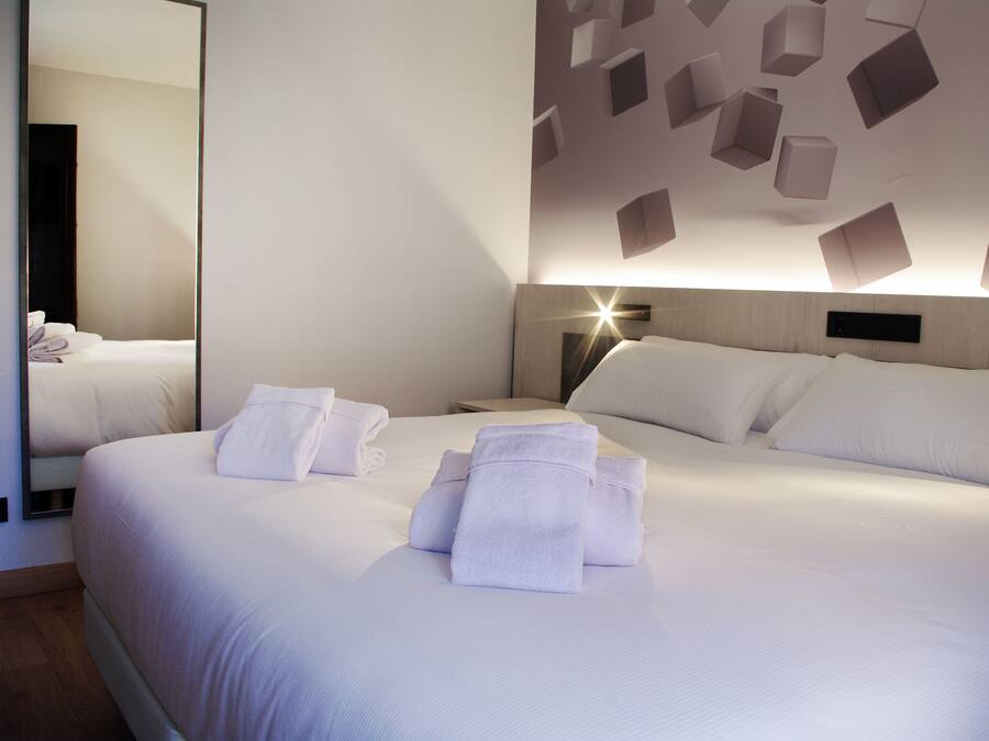 Ein Hotelzimmer mit einem großen Bett, einem Nachttisch, einem Spiegel und einer Wand mit geometrischen Leuchten.