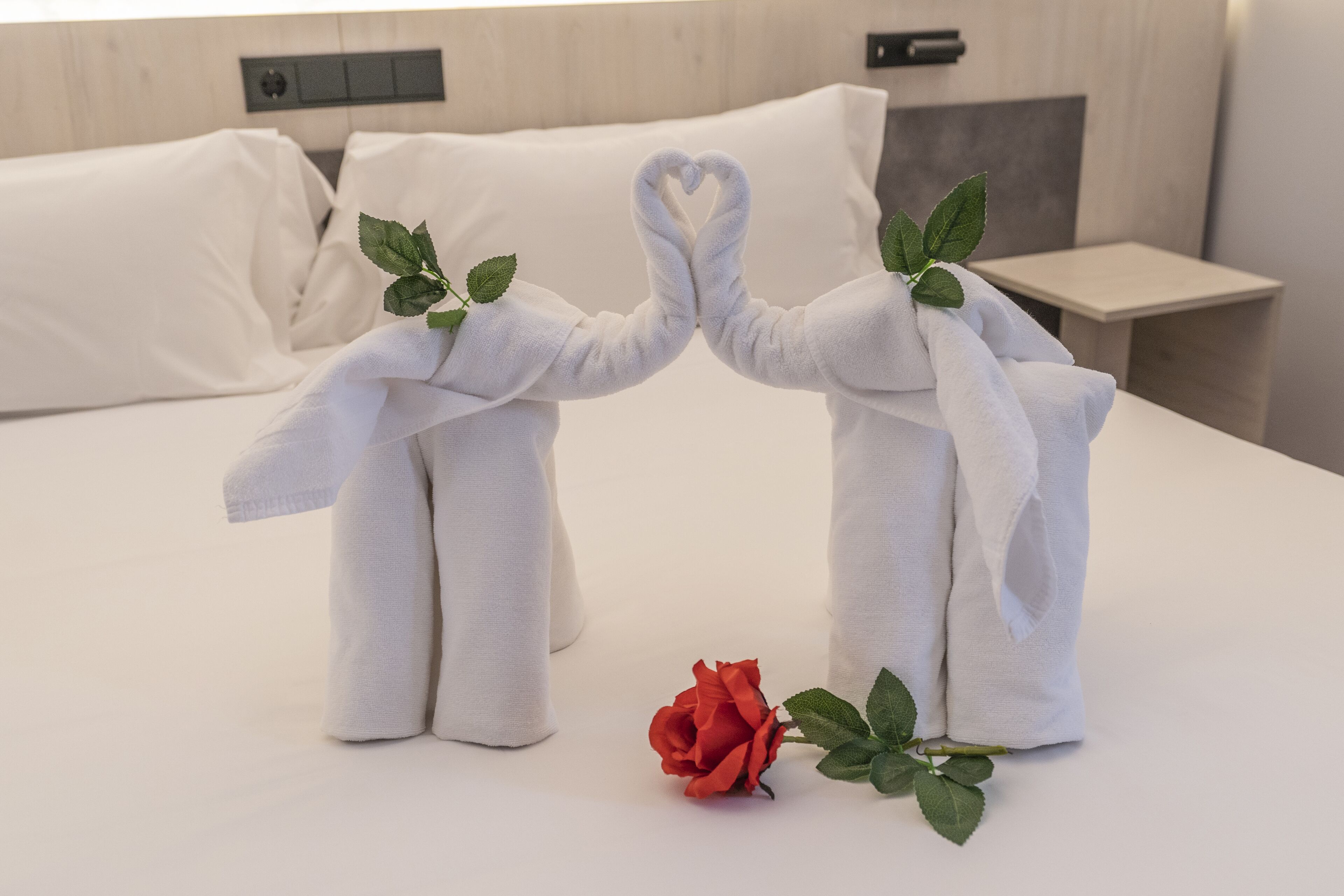 Ein Bett mit weißer Bettwäsche, eine rote Rose und zwei Handtücher in Form von Elefanten mit Blättern.