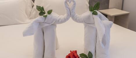 Ein Bett mit weißer Bettwäsche, eine rote Rose und zwei Handtücher in Form von Elefanten mit Blättern.