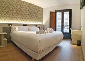A modern hotel room with a large bed, a bedside table, a desk, and a view of the city through a large window. - Hotel NERU con encanto (León)
