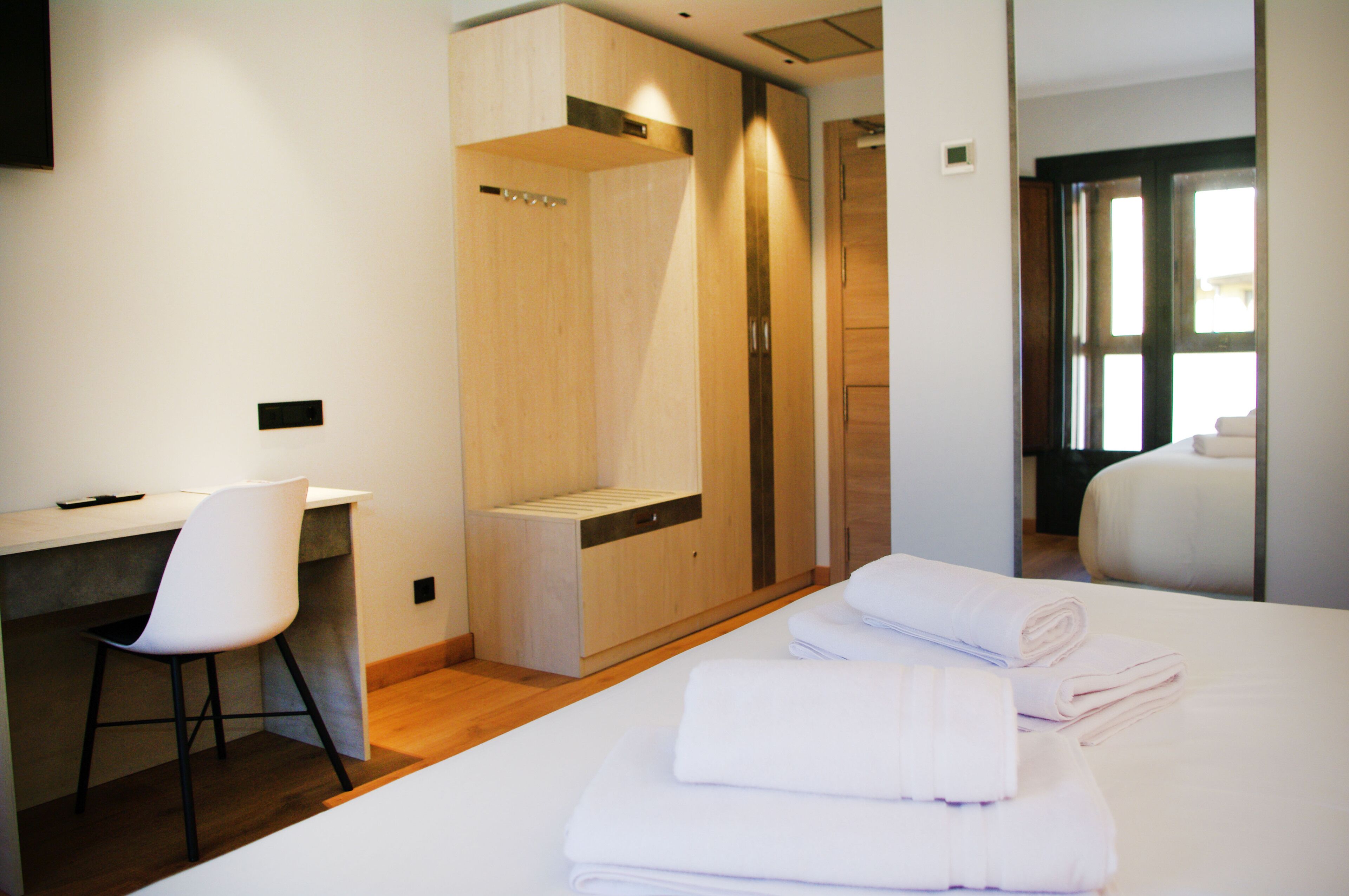Habitación de hotel con cama, escritorio, silla, armario y baño visible a través de una puerta abierta.