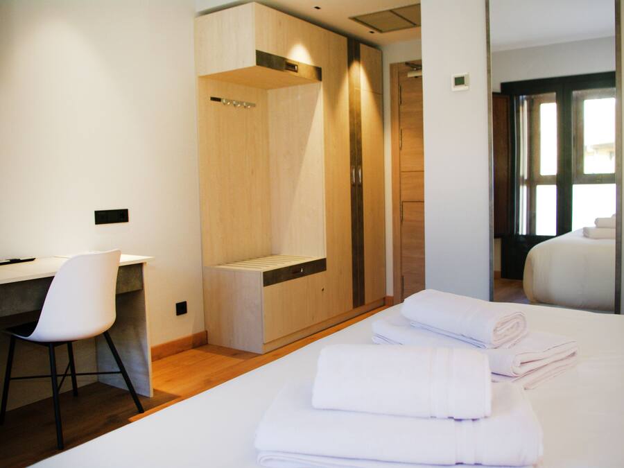Habitación de hotel con cama, escritorio, silla, armario y baño visible a través de una puerta abierta.