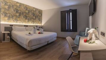 Una habitación de hotel moderna con una cama grande, un escritorio, una silla, un televisor de pantalla plana y un cuadro abstracto de gran tamaño en la pared.