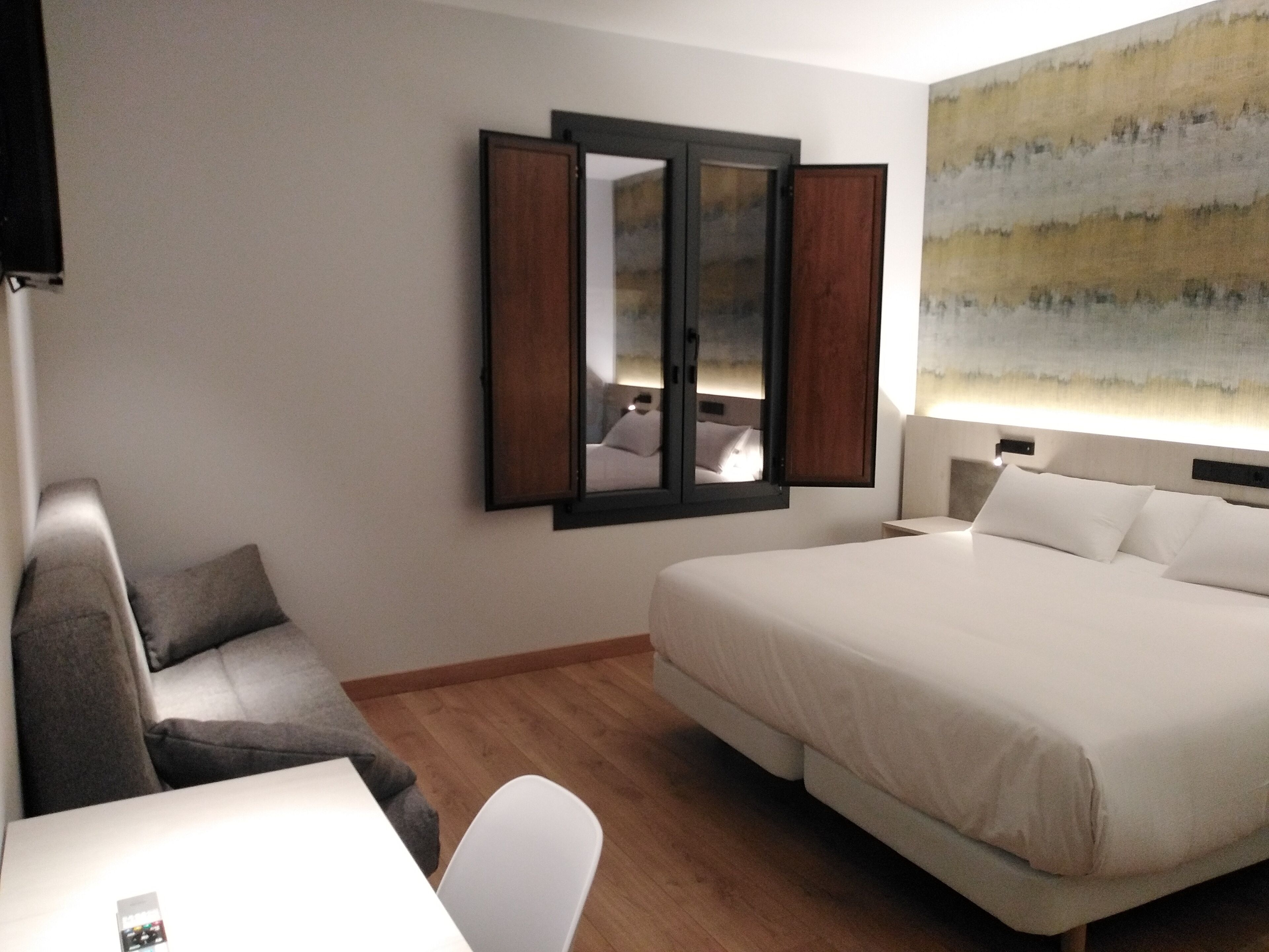 A hotel room with a bed, a desk, a chair, and a large window with a view.