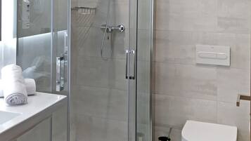 Un baño moderno con cabina de ducha de vidrio, inodoro y lavamanos con una toalla.
