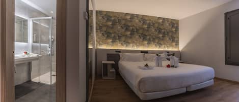 A modern hotel room with a large bed, a glass shower enclosure, and a textured wall mural.
