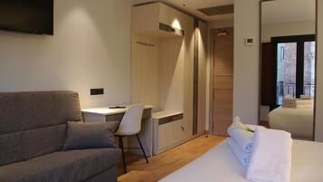 Habitación de hotel moderna con un sofá gris, un escritorio pequeño, un armario y una cama con una toalla blanca.