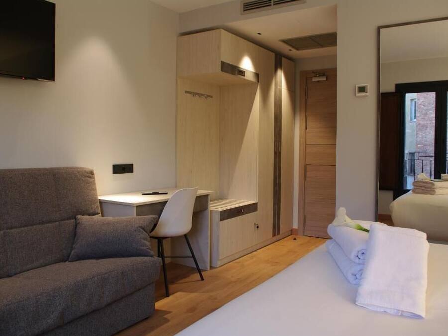 Habitación de hotel moderna con un sofá gris, un escritorio pequeño, un armario y una cama con una toalla blanca.