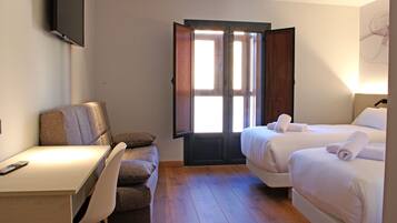 Habitación de hotel con escritorio, dos camas, una silla y un ventanal grande.