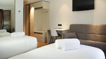 A hotel room with two beds, a desk, a chair, and a TV.