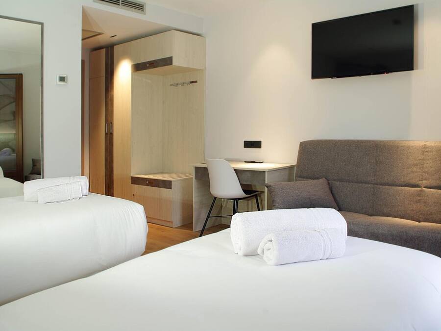 A hotel room with two beds, a desk, a chair, and a TV.
