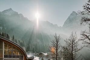 A mountain cabin with a view of snow-covered peaks and a forested valley.