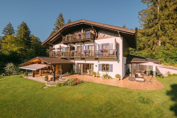Un chalet de dos pisos con balcón, un porche cubierto y un césped bien cuidado.