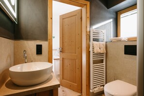 A bathroom with a large oval sink, a wooden door, a white toilet, and a towel rack.
