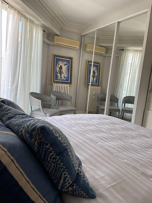 A bedroom with a large bed, two chairs, a mirror, and artwork on the wall.