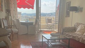 A living room with a red rug, a sofa, a coffee table, and a view of the city through a large window. - Perfect location at Promenades des Anglais, with balcony and a sea view. (Nice)