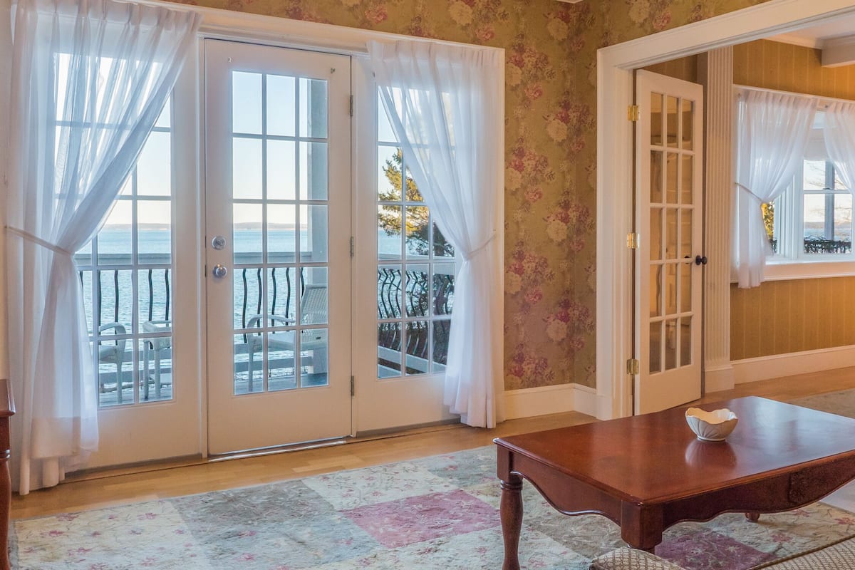 Una habitación con una mesa de madera, un tapete estampado y vista al mar a través de un ventanal.