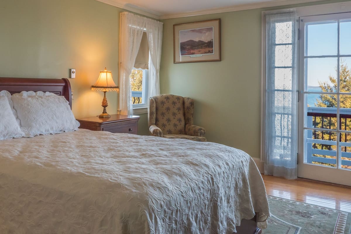 Un dormitorio con una cama grande, una mesita de noche con lámpara, una silla y una ventana con vistas.