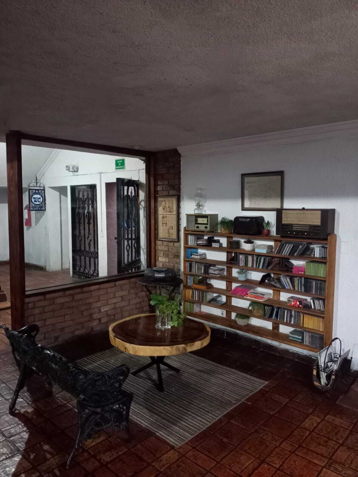 A room with a brick wall, a bookshelf, a round table with a plant, and a chair.