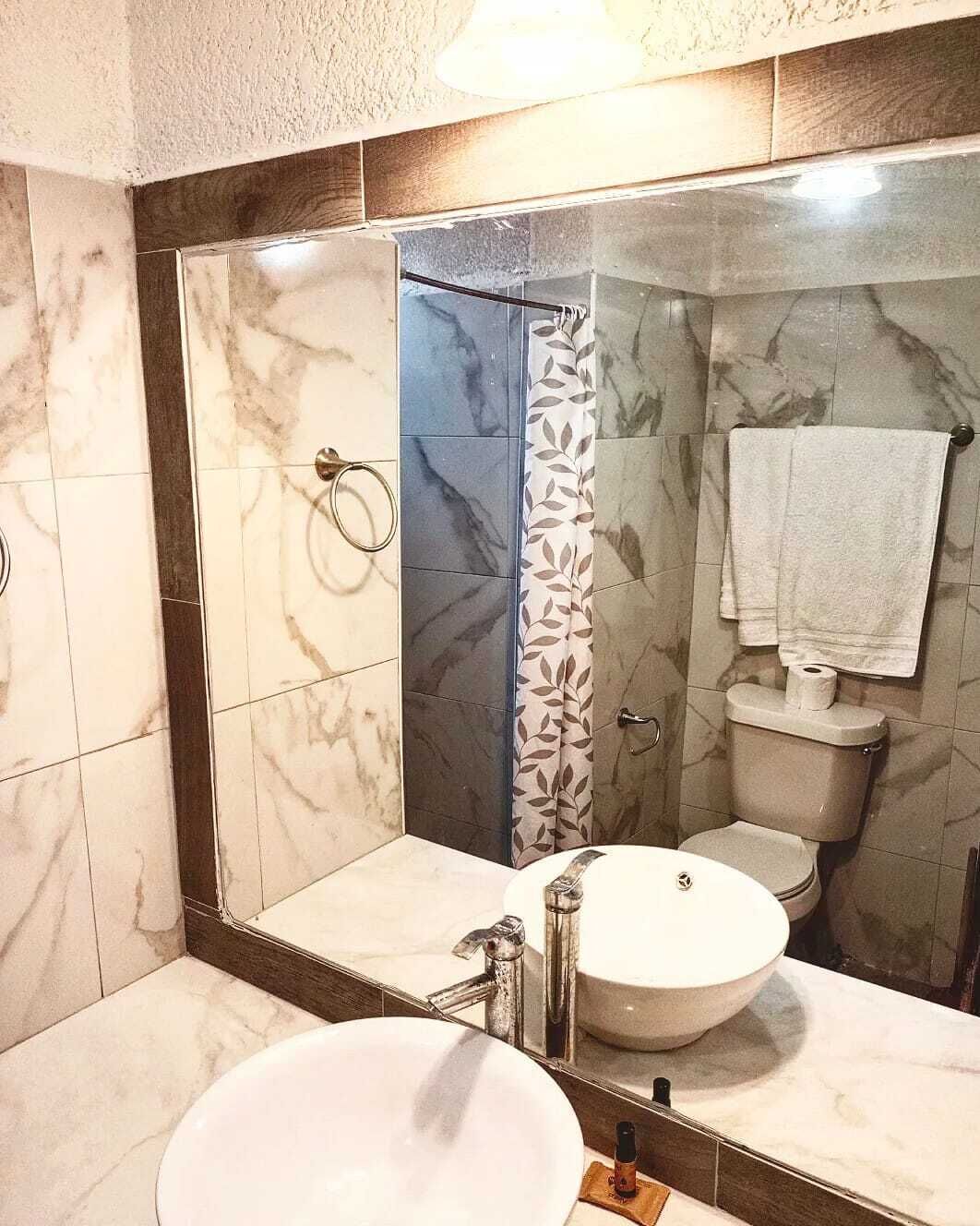 Un baño con lavamanos de mármol, inodoro y ducha con cortina estampada con hojas.