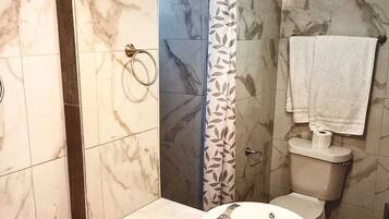Un baño con lavamanos de mármol, inodoro y ducha con cortina estampada con hojas.