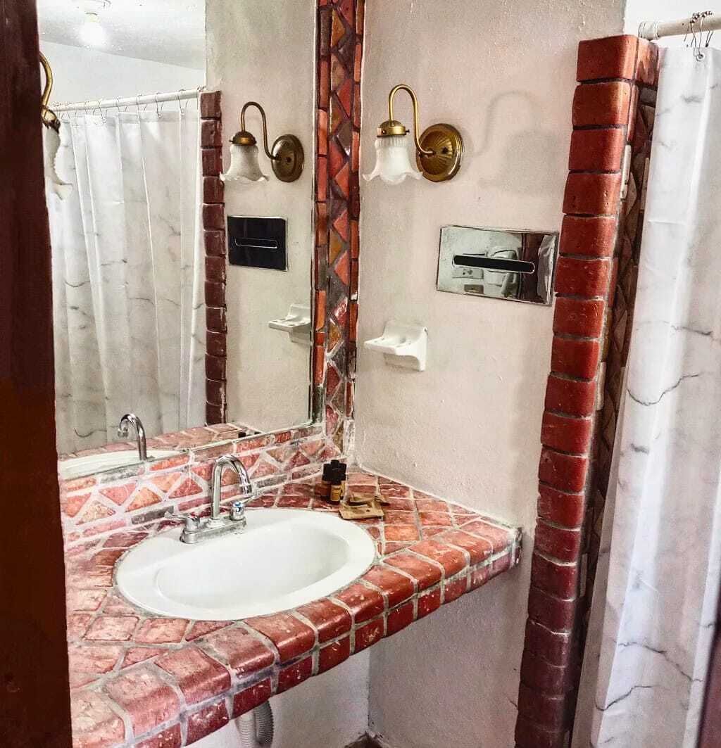 A bathroom with a tiled sink, a mirror, a shower curtain, and a wall-mounted light fixture.