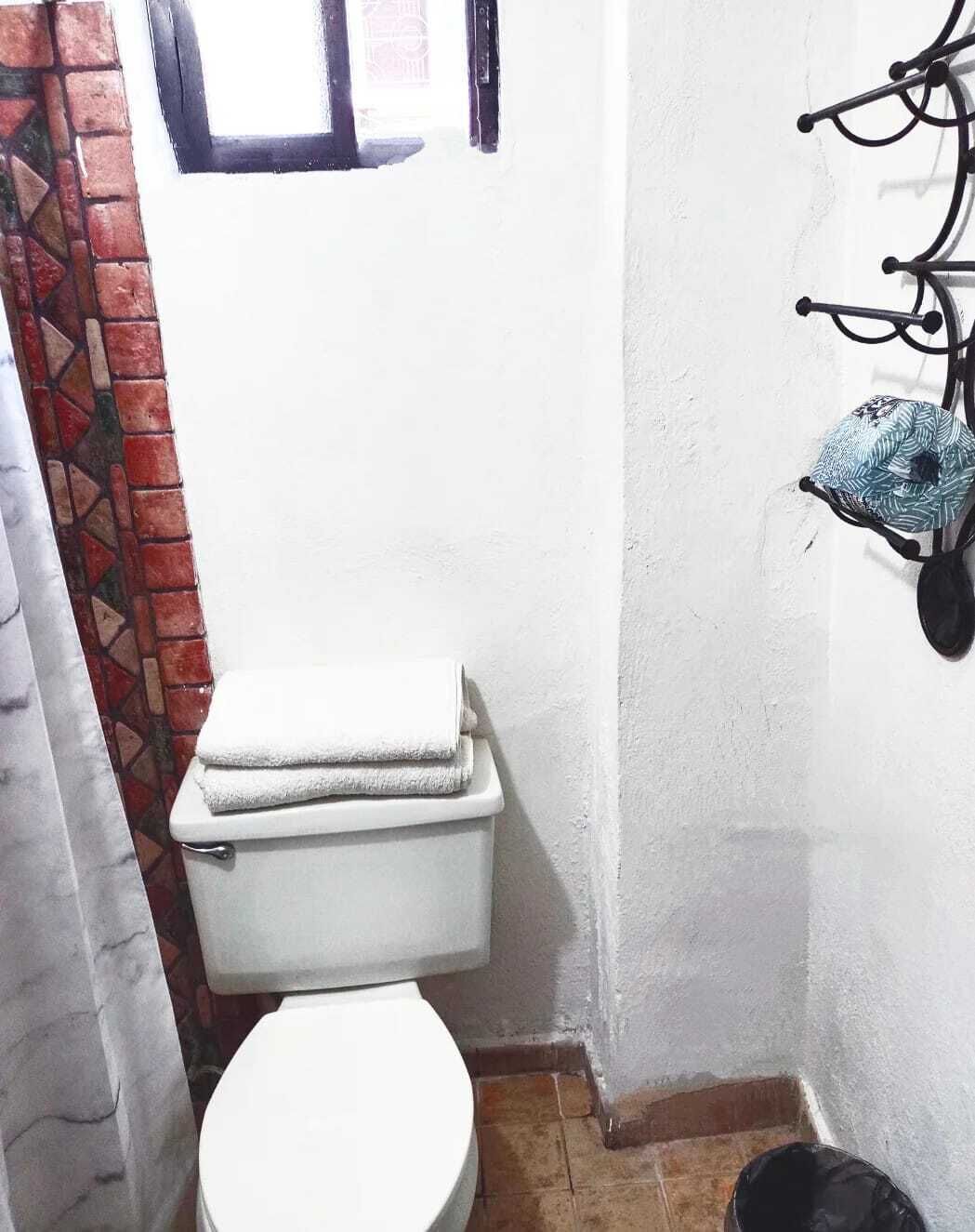 A small bathroom with a white toilet, a tiled floor, and a window with a black frame.