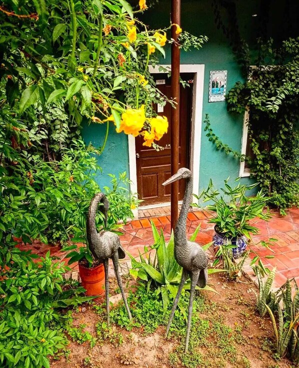 A courtyard with two stone sculptures of birds, surrounded by lush greenery and a door with a number 111 sign. - Hotel Olimpia Centro Histórico (Monclova)