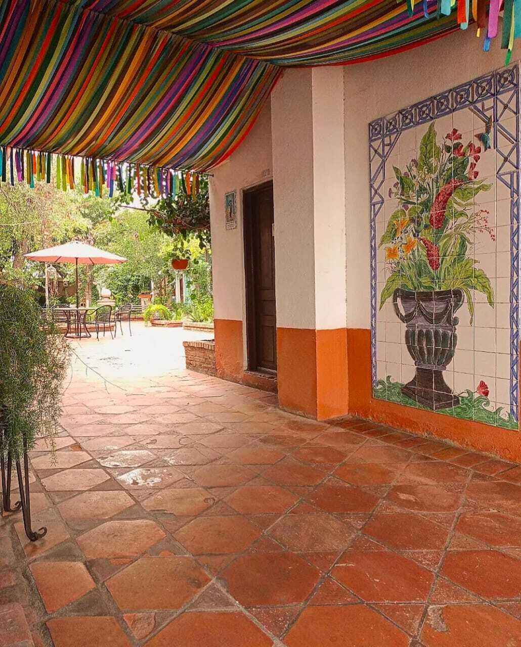 Una zona patio coperta, con pavimento piastrellato, un murale raffigurante una pianta in vaso e mobili da esterno.