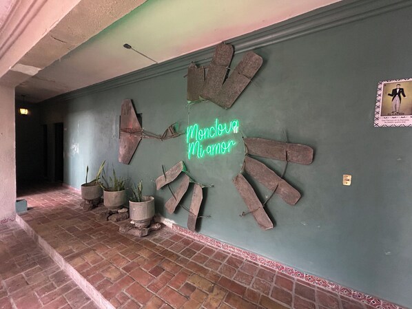 A hallway with a green wall, a neon sign reading "Mundo Amor", and several potted plants.