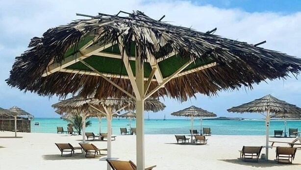 A beachside setting with a round wooden table and four chairs, surrounded by thatched umbrellas. - costa do sol (Boa Vista)